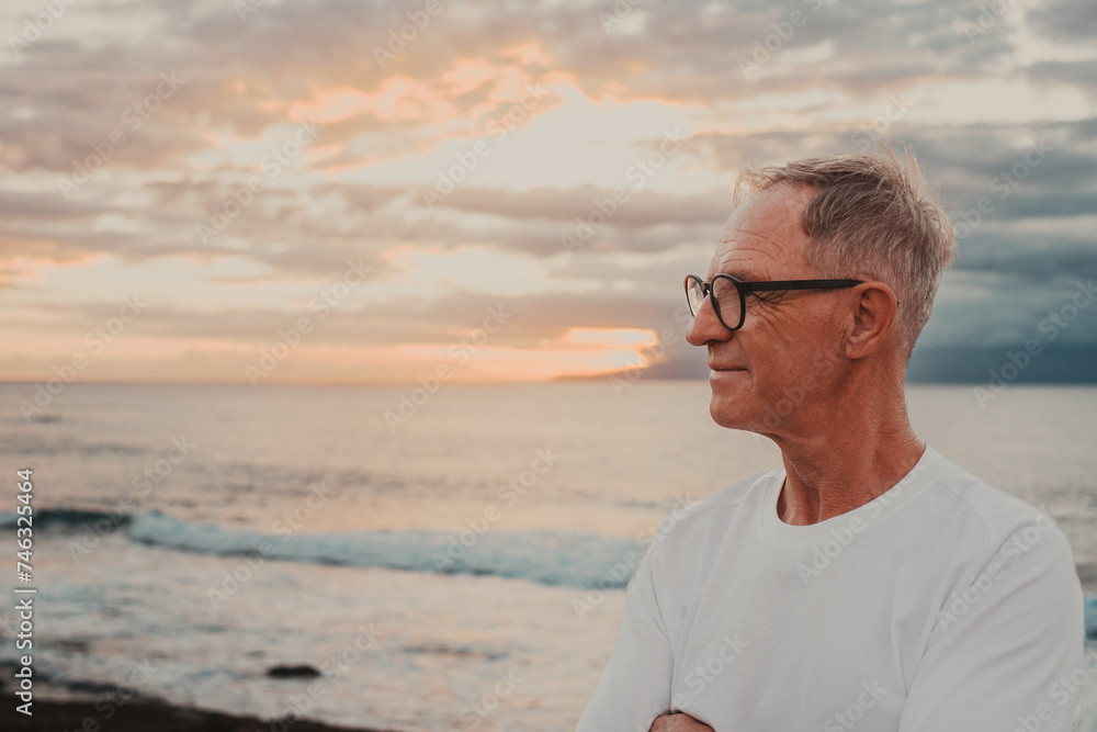 Senior mature man at the sea beach at sunset light looking the horizon over sea appreciating freedom and nature, handsome man enjoys a relaxed retirement lifestyle