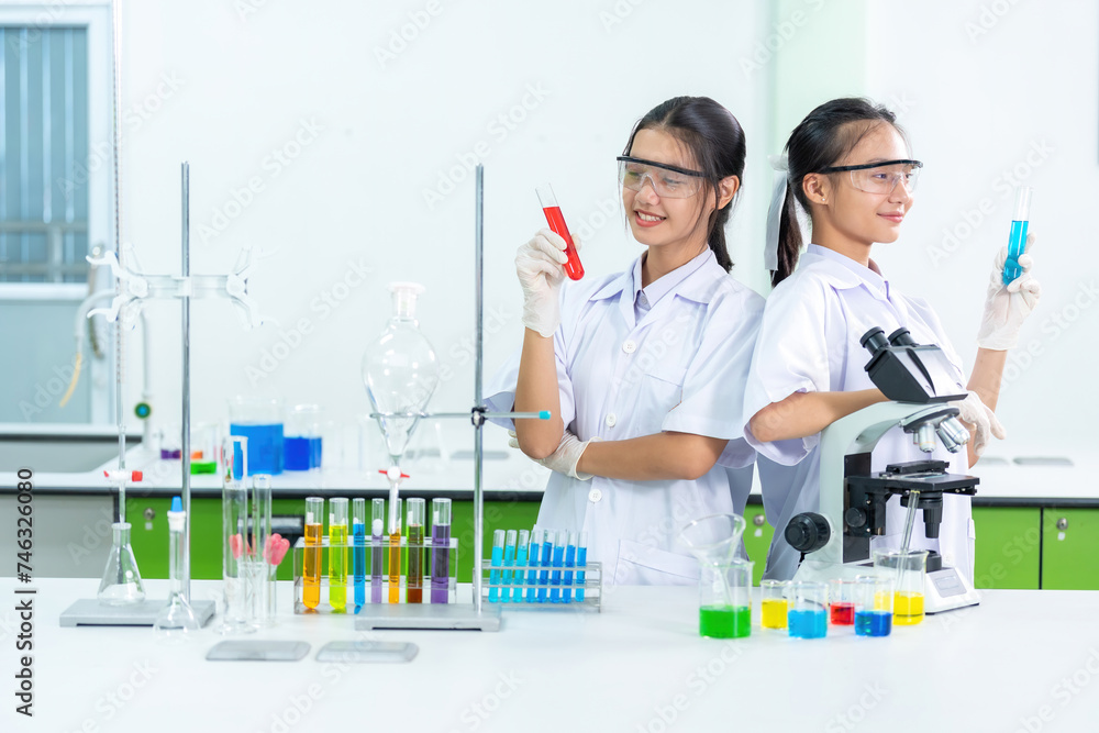 The presenters of the Faculty of Medicine are two Asian female students holding test tubes as they research chemical viral medicines using a microscope. There are beakers in the science lab.