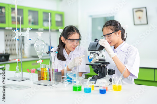 Two Asian female researchers Use and point at the microscope to test chemicals in the biology lab in the Ministry of Science. On the table are equipment such as pipers to produce medical vaccines.