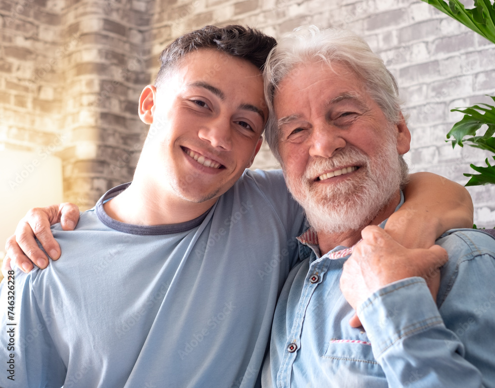 Portrait of family couple, a young boy and his old grandfather smiling looking at camera while sitting on the sofa at home, old and new generation - caring for the people we love