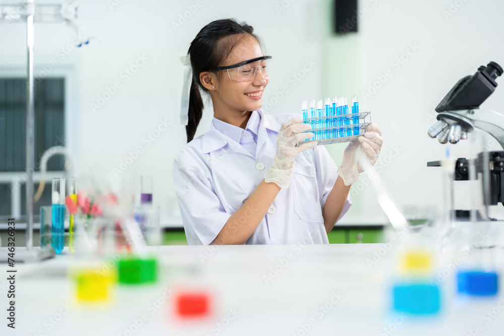 In a business company producing vaccines and medicines, medical industry and scientific business, there is an Asian female doctor holding a test tube. On the table was a microscope and a beaker. In a business company producing vaccines and medicines, medical industry and scientific business, there is an Asian female doctor holding a test tube. On the table was a microscope and a beaker.