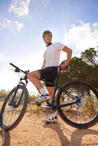 Fototapeta Naklejka Na Ścianę i Meble -  Cyclist, man and bicycle ride in outdoors, hill and mountain biking in countryside. Male person, freedom and cardio for fitness or exercise, hobby and sports for adventure and off road by blue sky