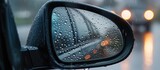 A modern cars left wing mirror is shown in the image, covered with rain drops. The water droplets obstruct the mirrors reflective surface, affecting the drivers ability to see the rear view.