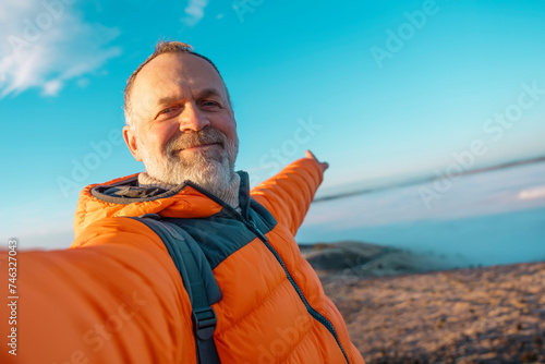 Happy elderly  mature man enjoying life at full by travelling around world sitting on the top of mountains against sky and clouds on cold sunny winter soring day. Travel Lifestyle concept photo