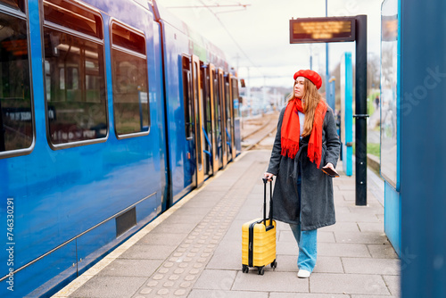 Happy tourist woman with small yellow luggage at the train station exited about oncoming journey. Enjoying travel by train concept