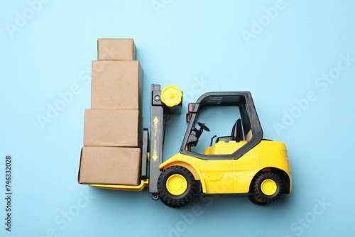 Top view of toy forklift with boxes on blue background, space for text. Logistics and wholesale concept