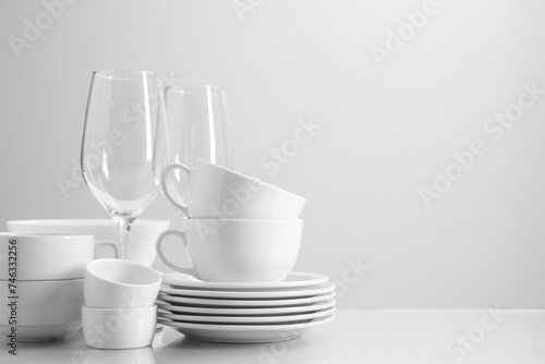 Set of many clean dishware and glasses on light table. Space for text