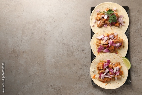 Delicious tacos with vegetables, meat and lime on grey textured table, top view. Space for text