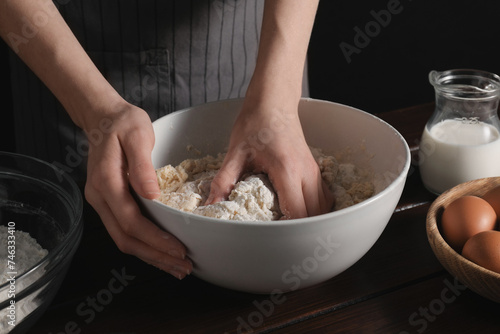 Making bread. Woman kneading dough at wooden table on dark background, closeup