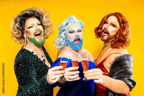 Trio of drag queens in elegant attire having a toast with red wine