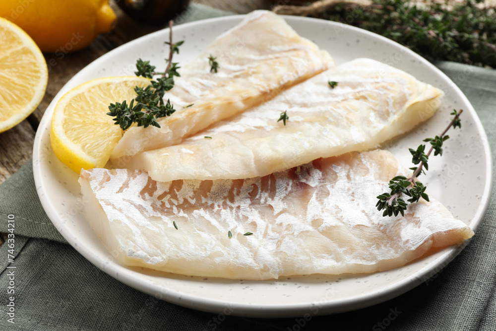 Fresh raw cod fillets with thyme and lemon on table, closeup
