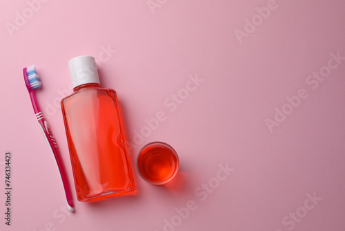 Fresh mouthwash in bottle, glass and toothbrush on pink background, flat lay. Space for text