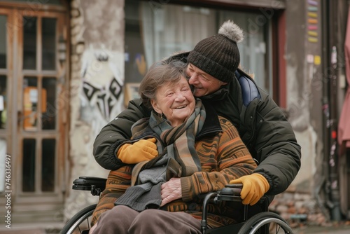 Elderly woman in wheelchair laughing with man outside, both wearing warm clothes