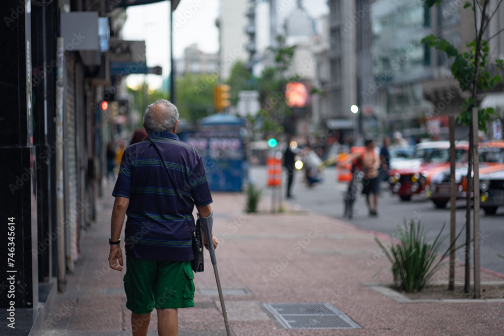 An elderly man walking on the sidewalk with a cane.