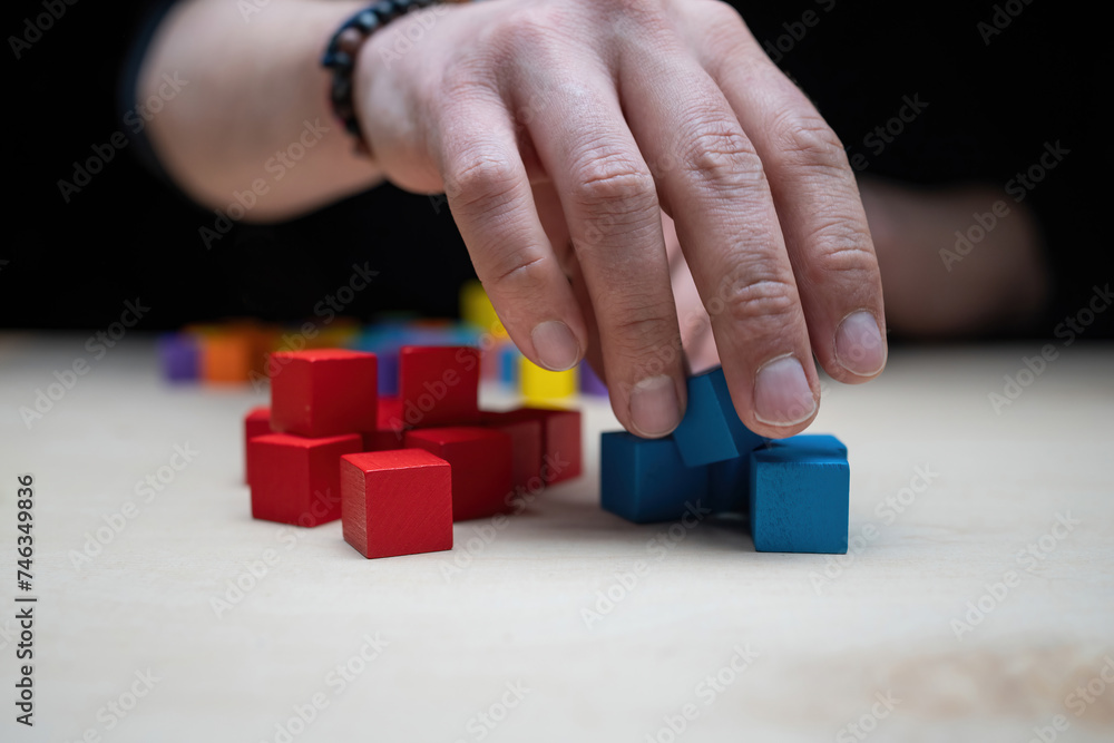 Hands stacking colored wooden blocks onto a table by color
Hands stacking colored wooden blocks onto a table by color