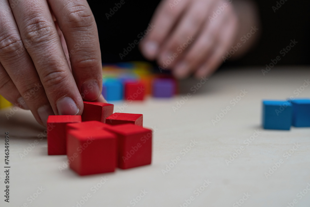 Hands stacking colored wooden blocks onto a table by color
Hands stacking colored wooden blocks onto a table by color