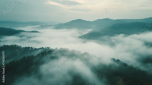 Aerial forest mountains landscape in the morning light with lots of low clouds hooked to the highest forest trees and an hazy sky