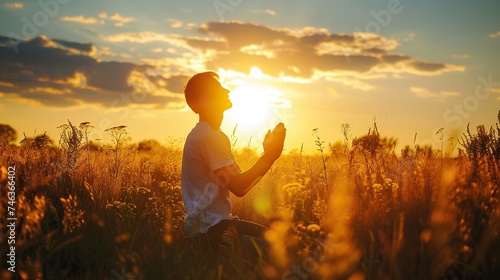 Young man praying in the meadow at sunset