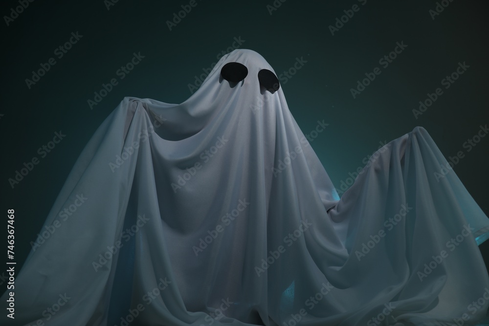Creepy ghost. Woman covered with sheet on dark teal background, low angle view