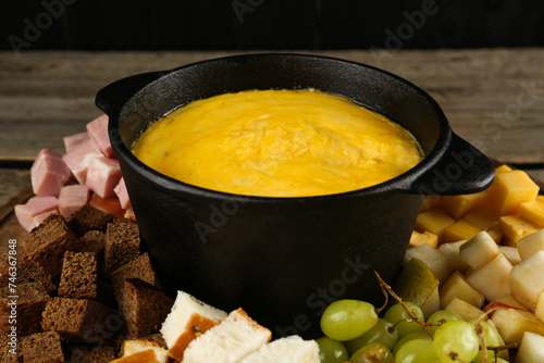 Fondue pot with melted cheese and different products on table, closeup