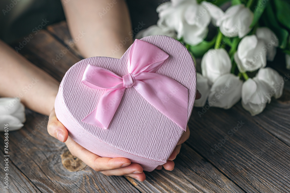 Gift box in the shape of a heart in a female hands on a wooden background.