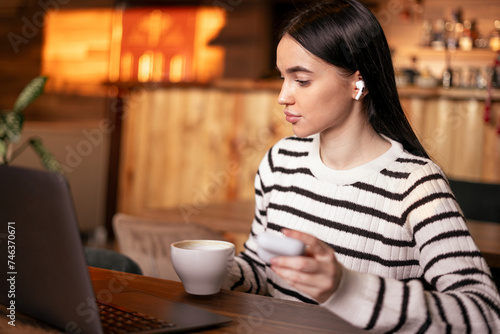 A beautiful woman with long hair holds headphones in her hands and works in a cafe using a laptop and a wireless connection. Remote work and business concept