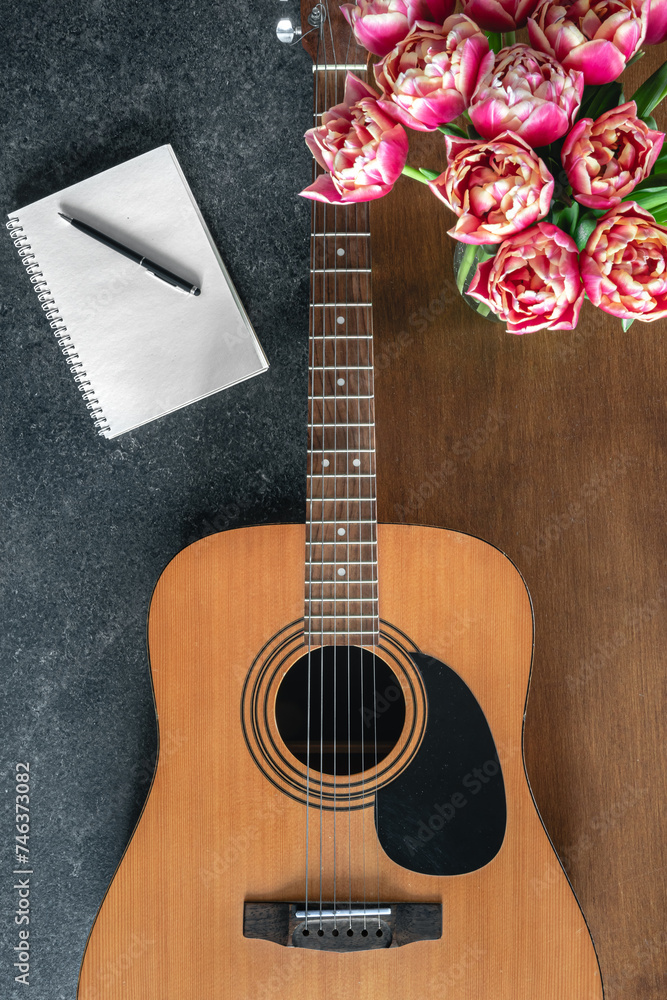 Fototapeta premium Top view, acoustic guitar, notepad and tulips on the table.