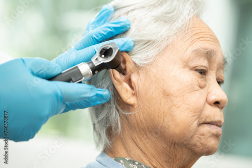 Audiologist or ENT doctor use otoscope checking ear of asian senior woman patient treating hearing loss problem.