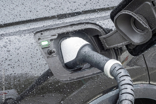A close-up image of an electric vehicle with a charging point plugged into the car and re-charging the vehicle. photo