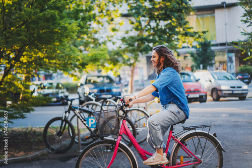 A young happy Caucasian woman rides a bicycle to a public bicycle parking lot in a summer city