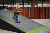 child preschooler kid boy rides a scooter in the park on a skateboard ramp in the autumn