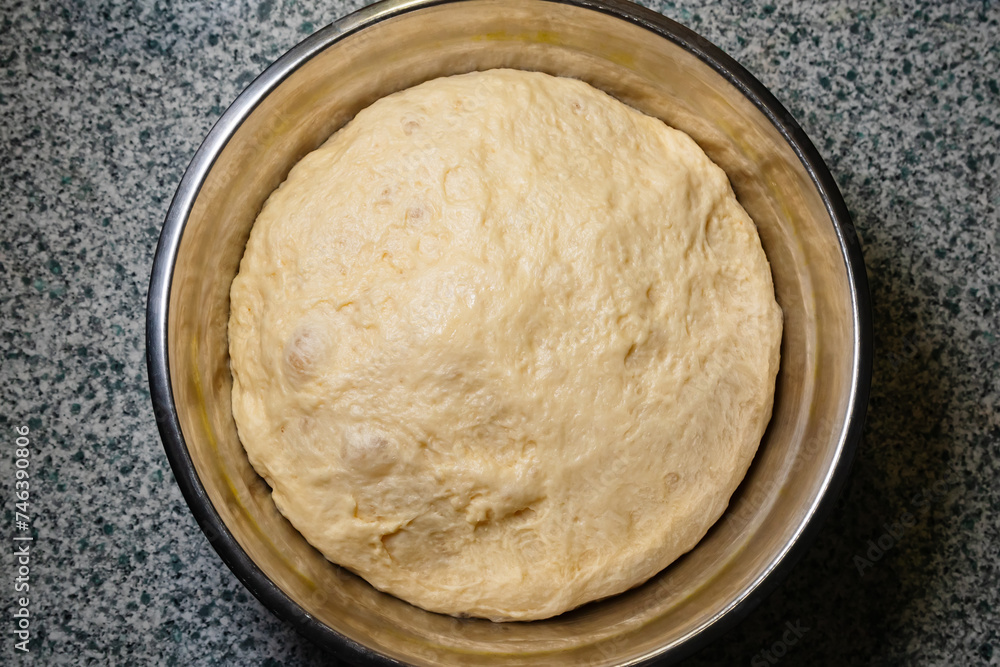 Raw dough for bread or buns made from white flour in an iron plate on the table, top view of baking ingredient
