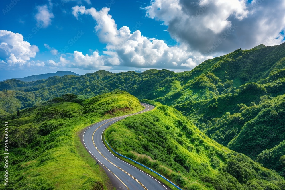 Aerial view of an empty mountain highway weaving through lush green hills on a sunny day, with vibrant blue skies and fluffy white clouds. Aerial view of an empty mountain highway weaving through lush green hills on a sunny day, with vibrant blue skies and fluffy white clouds.