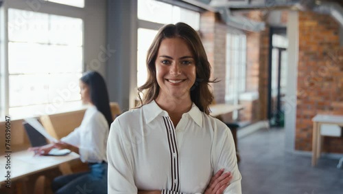 Portrait of smiling young businesswoman working in modern open plan office turning to look at camera and folding arms - shot in slow motion photo