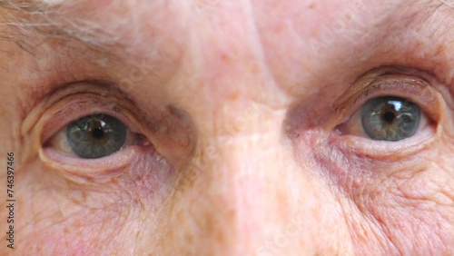 Elderly woman watching into camera and strongly screwing up her eyes. Close up of wrinkled female face with wide eyes showing surprise emotions. Granny with amazed facial expression. Slow motion photo