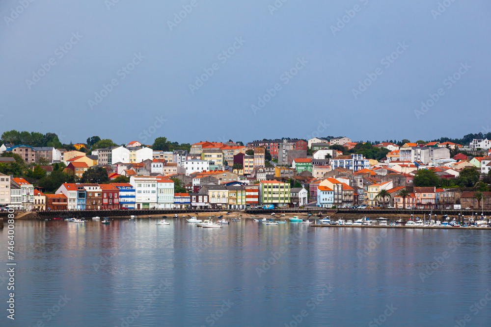The coast of the Spanish city of Feroll with colorful houses near the water and yachts at the piers.