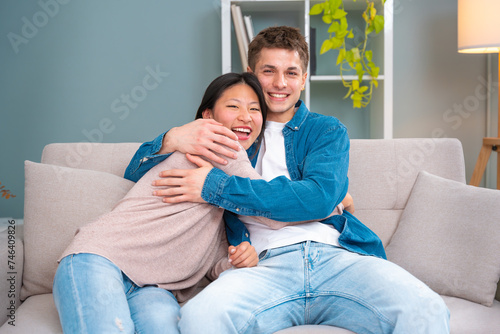 Happy young multiracial couple hugging sitting on the sofa in the living room.