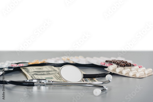 stethoscope and blisters of pills surrounding cash dollars on a gray table with copy space background