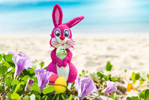 Pink Easter bunny holding green egg on tropical beach, Happy Easter card background idea