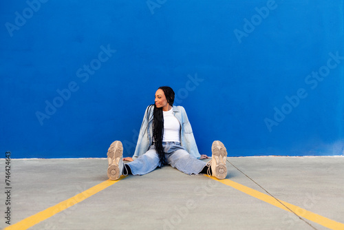 Smiling young woman sitting on floor in front of blue wall photo