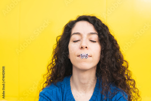 Woman with butterfly sticker on lip against yellow background photo