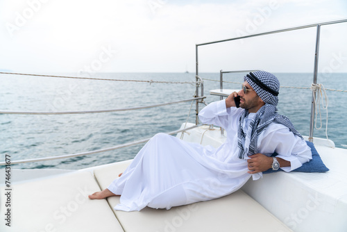 Arab businessman speaking on mobile phone working corporate business during travel on private catamaran boat yacht sailing in the ocean. Arabic man enjoy luxury outdoor lifestyle on summer vacation. © CandyRetriever 