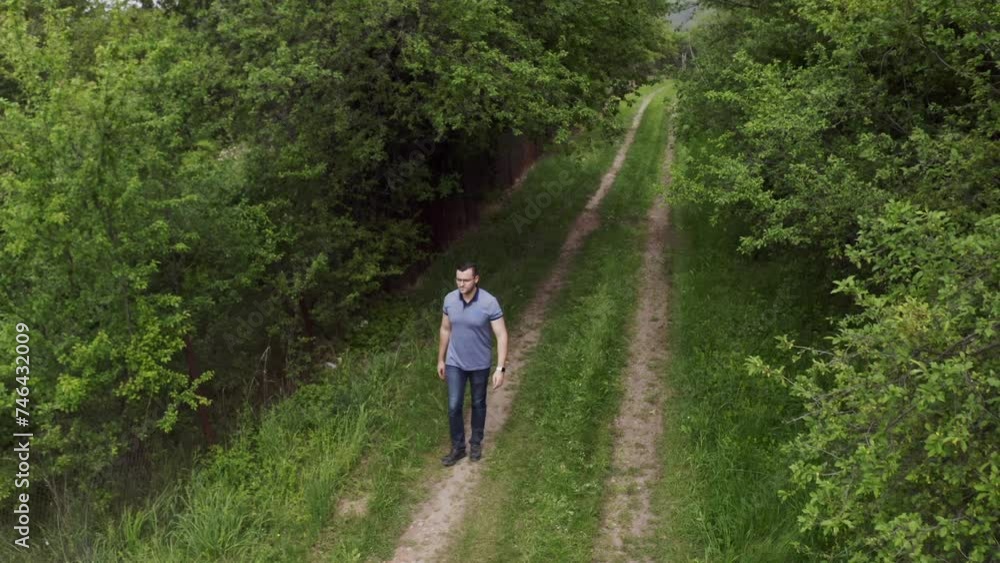 Retreating drone shot of a tourist walking on a dirt road in the woodlands of Tsarichina Hole Village in a remote countryside in Bulgaria. Retreating drone shot of a tourist walking on a dirt road in the woodlands of Tsarichina Hole Village in a remote countryside in Bulgaria.