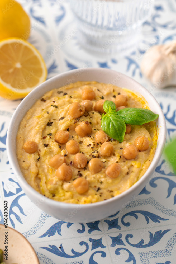 A bowl of hummus with chickpeas and basil on a table A bowl of hummus with chickpeas and basil on a table
