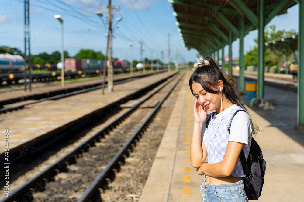 Young Asian woman enjoy and fun outdoor lifestyle road trip travel by railway transportation on summer holiday vacation. Attractive girl walking on railroad track during waiting for train at station.