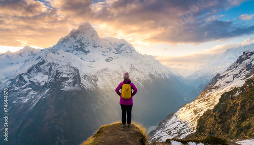A female hiker standing at sunrise admiring the view of a snow covered mountain range