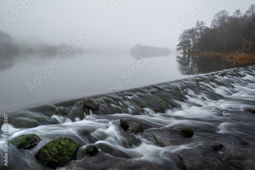 Flowing water at Grasmere weir on a misty morning in The Lake District, UK.