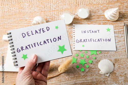 Person hand choosing delayed gratification instead of easy instant gratification. Text on notepad decorated with seashells indoors studio shot.