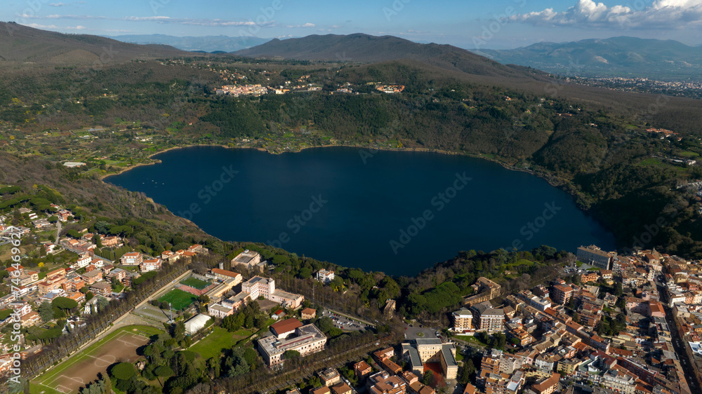 Aerial view of Lake Nemi. It is a small volcanic lake in the territory of the Castelli Romani. In foreground it is Genzano di Roma, a small town located in the Metropolitan City of Rome, Italy. 