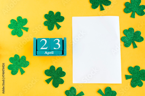 April 23. Blue cube calendar with month and date and white mockup blank on bright yellow background.